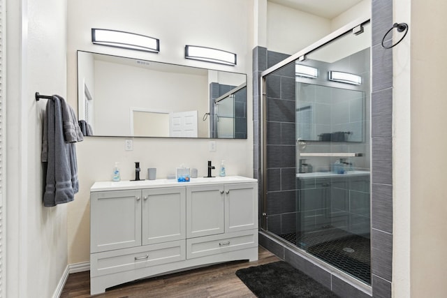 bathroom with wood finished floors, baseboards, double vanity, a sink, and a shower stall