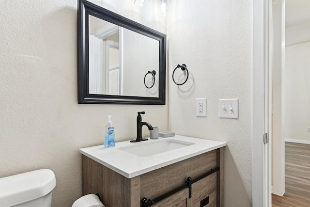 half bath featuring vanity, toilet, and wood finished floors