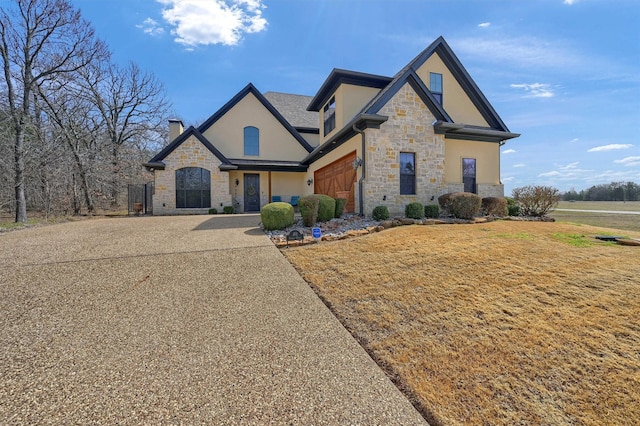 view of front of home with an attached garage, a front yard, stucco siding, stone siding, and driveway