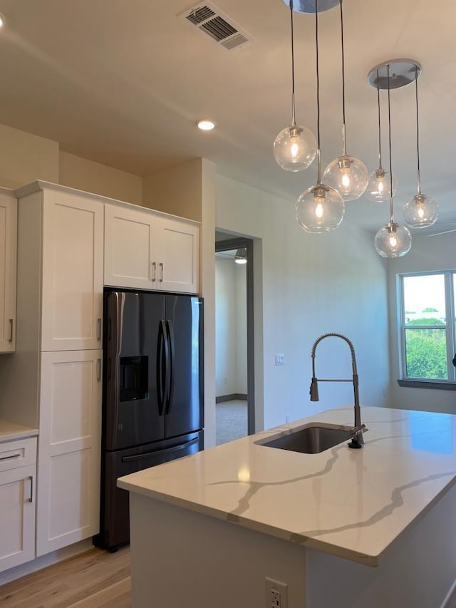 kitchen with a sink, a center island with sink, white cabinetry, and black refrigerator with ice dispenser