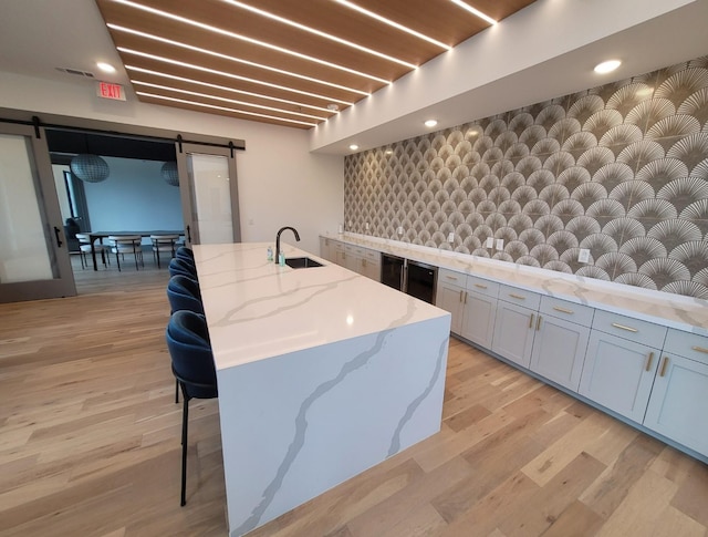 kitchen featuring a kitchen bar, a kitchen island with sink, a sink, a barn door, and light wood finished floors