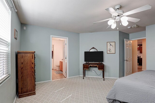 bedroom with ensuite bath, light colored carpet, baseboards, and ceiling fan