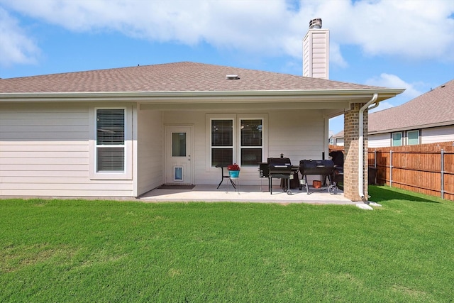 rear view of house with fence, roof with shingles, a yard, a chimney, and a patio area