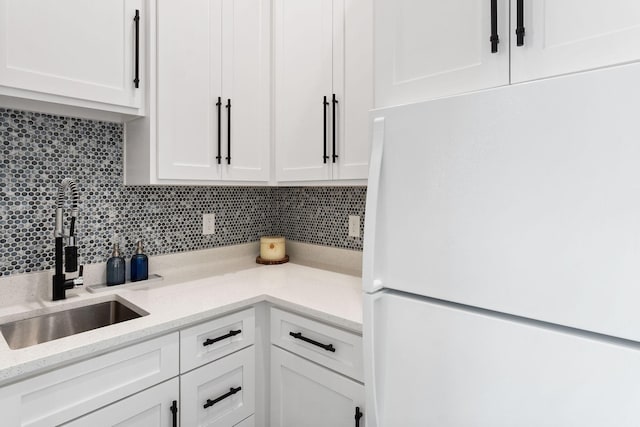 kitchen featuring backsplash, white cabinets, freestanding refrigerator, and a sink