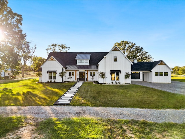 modern farmhouse featuring a front yard, a standing seam roof, gravel driveway, board and batten siding, and metal roof