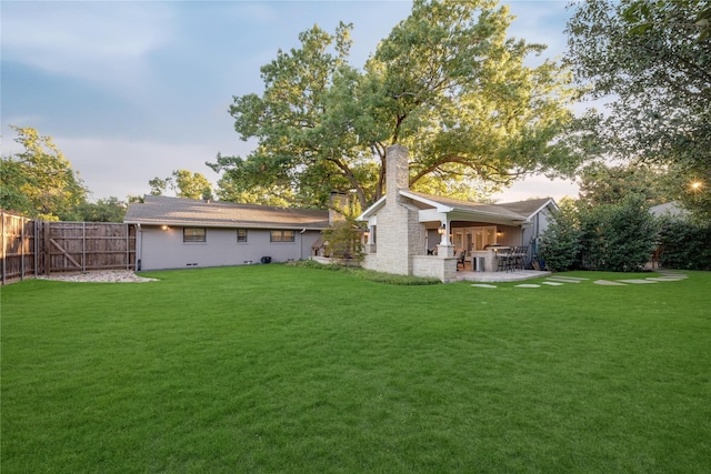 back of house with a yard, a patio area, fence, and a chimney