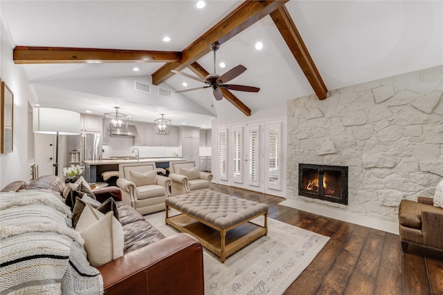 living area with visible vents, hardwood / wood-style floors, beam ceiling, a stone fireplace, and a ceiling fan