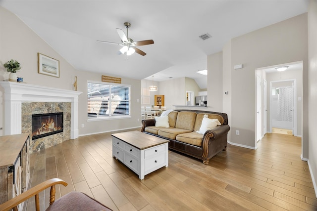 living area with visible vents, light wood-style flooring, ceiling fan, vaulted ceiling, and a tiled fireplace