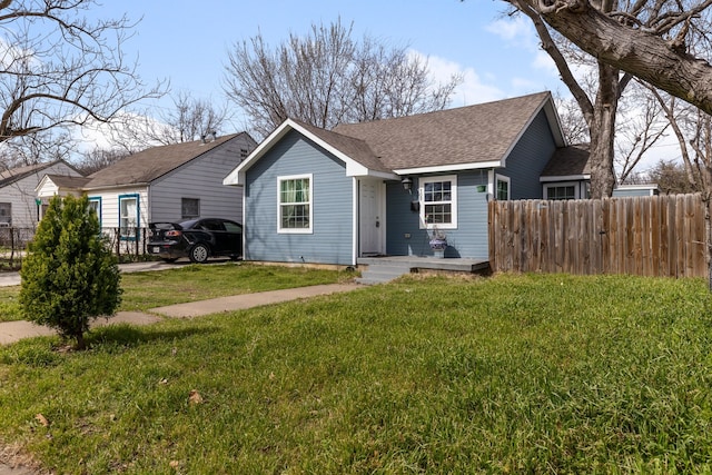 view of front of house featuring roof with shingles, a front lawn, and fence