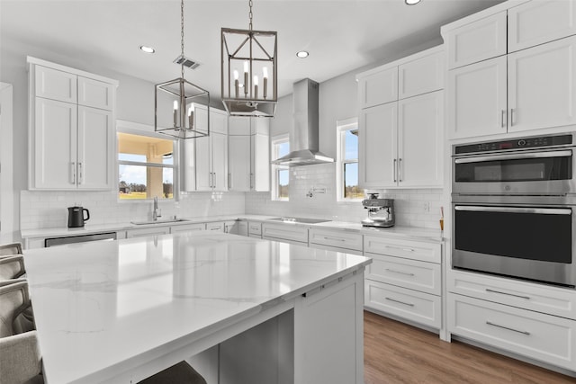 kitchen with visible vents, a breakfast bar, a sink, stainless steel appliances, and wall chimney range hood