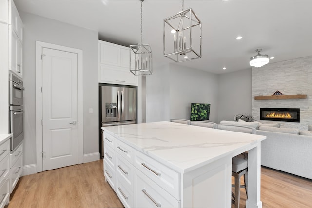 kitchen featuring light stone counters, a kitchen island, appliances with stainless steel finishes, white cabinetry, and light wood-type flooring