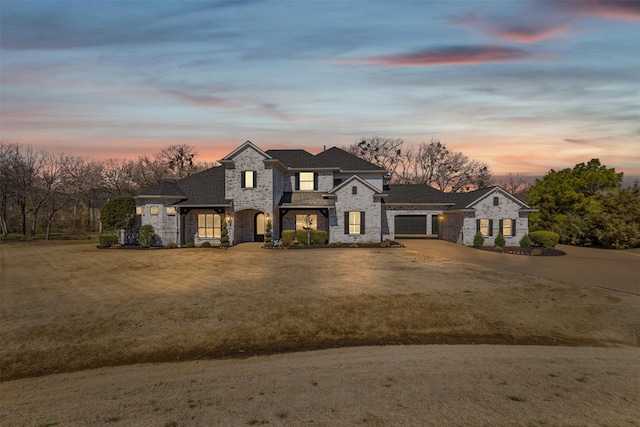 french country home featuring stone siding, an attached garage, concrete driveway, and a yard