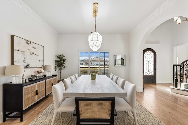 dining room featuring light wood-type flooring, stairway, arched walkways, crown molding, and baseboards