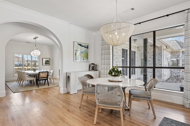 dining area with visible vents, an inviting chandelier, light wood-style flooring, arched walkways, and ornamental molding