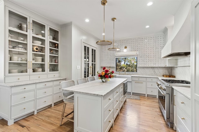 kitchen with a kitchen island, a breakfast bar, high end stove, custom range hood, and white cabinetry