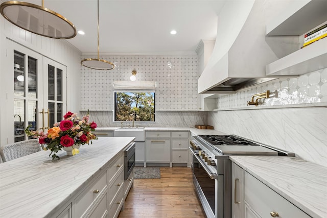 kitchen featuring light wood-type flooring, custom range hood, light stone counters, tasteful backsplash, and appliances with stainless steel finishes