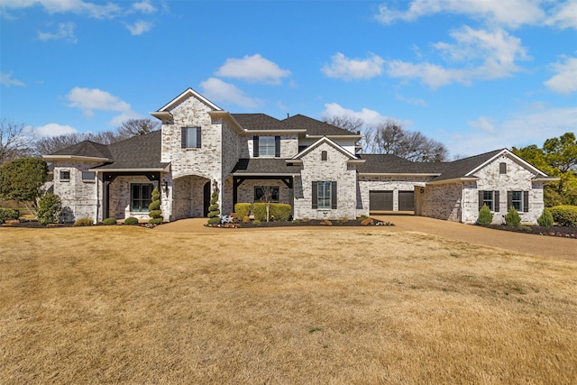 french country inspired facade with a front lawn, driveway, and roof with shingles