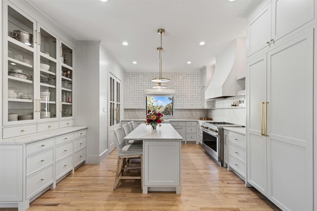 kitchen with a kitchen island, stainless steel range, custom range hood, glass insert cabinets, and light wood-style floors