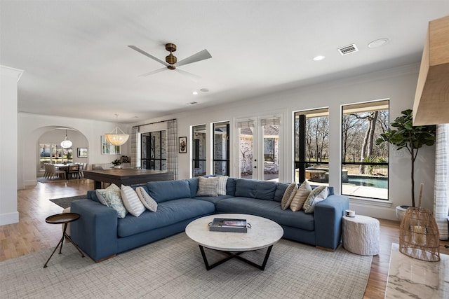 living area with visible vents, ornamental molding, recessed lighting, light wood-style floors, and arched walkways