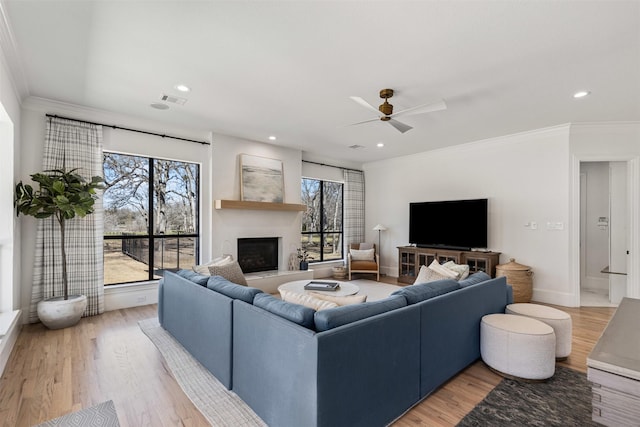 living room with a wealth of natural light, light wood finished floors, a fireplace, and ornamental molding