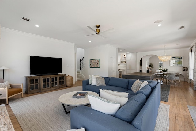 living area featuring arched walkways, light wood-style floors, ornamental molding, and stairs