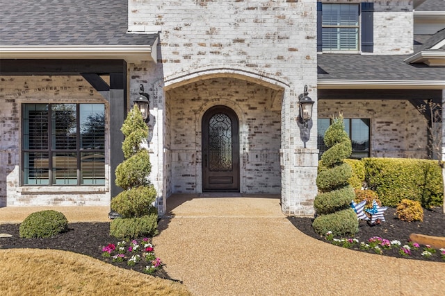 view of exterior entry featuring brick siding and a shingled roof