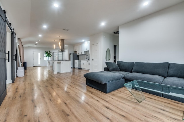 living room featuring visible vents, lofted ceiling, recessed lighting, light wood-style floors, and a barn door