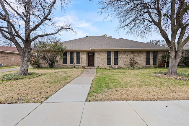 single story home featuring brick siding, a front yard, and a shingled roof