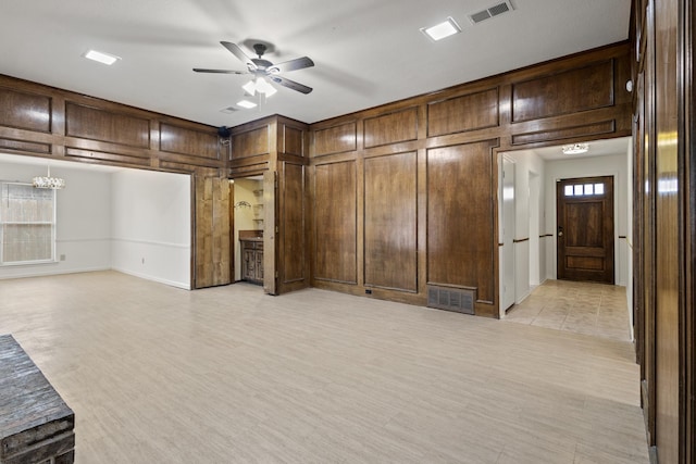 unfurnished living room featuring light wood finished floors, visible vents, wood walls, and ceiling fan