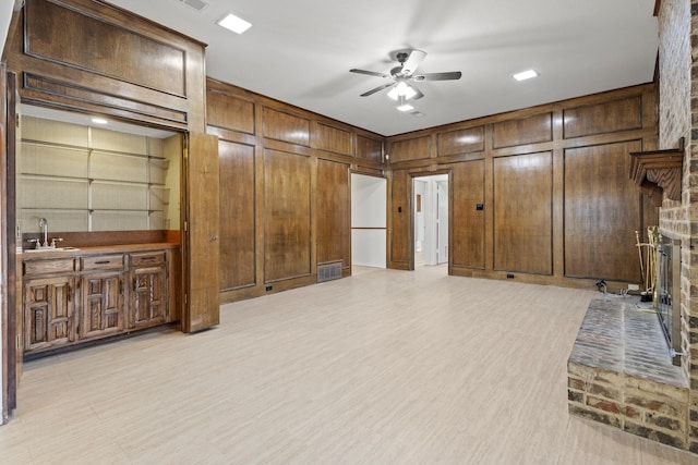 living room with wooden walls, visible vents, a large fireplace, light wood-type flooring, and a ceiling fan