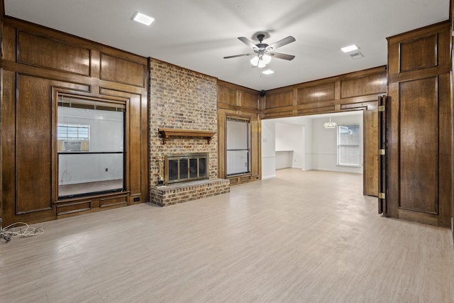 unfurnished living room with wooden walls, a fireplace, light wood-style floors, and ceiling fan