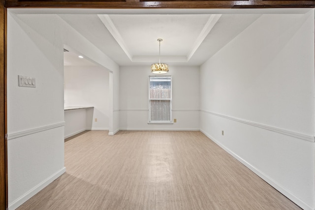 empty room with a tray ceiling, baseboards, and light wood finished floors