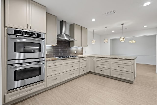 kitchen featuring visible vents, stainless steel appliances, a peninsula, wall chimney range hood, and decorative backsplash