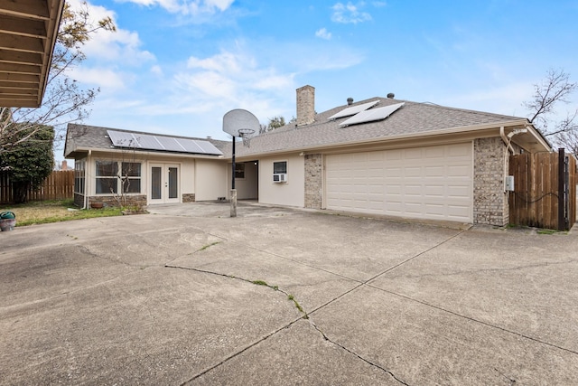 view of front facade featuring solar panels, concrete driveway, french doors, and fence