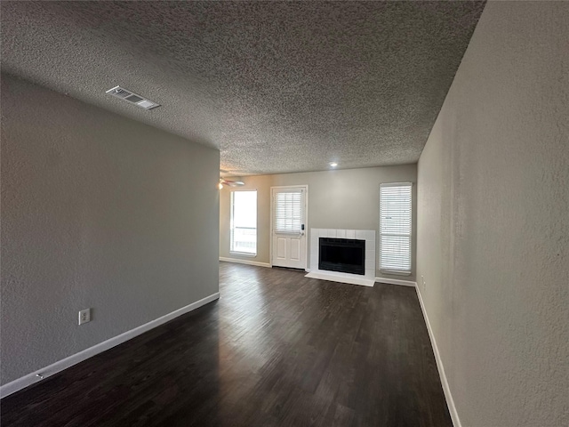 unfurnished living room with visible vents, a textured ceiling, a fireplace, baseboards, and dark wood-style flooring