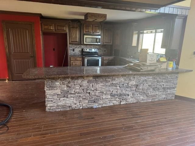 kitchen featuring decorative backsplash, a peninsula, appliances with stainless steel finishes, and wood finished floors