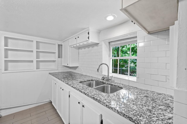 kitchen with light stone countertops, decorative backsplash, light wood-style floors, white cabinets, and a sink