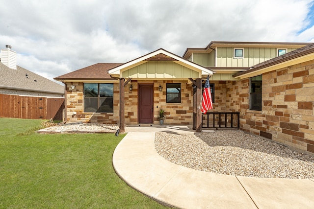 view of front of property featuring stone siding, board and batten siding, a front yard, and fence