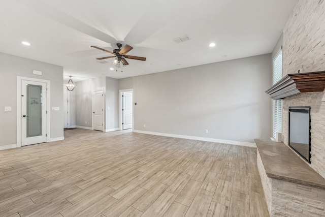 unfurnished living room with a stone fireplace, a ceiling fan, baseboards, and light wood finished floors