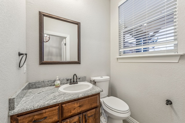 half bath with toilet, vanity, and a textured wall