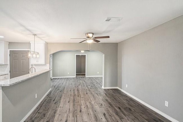 unfurnished living room with arched walkways, visible vents, dark wood finished floors, and baseboards