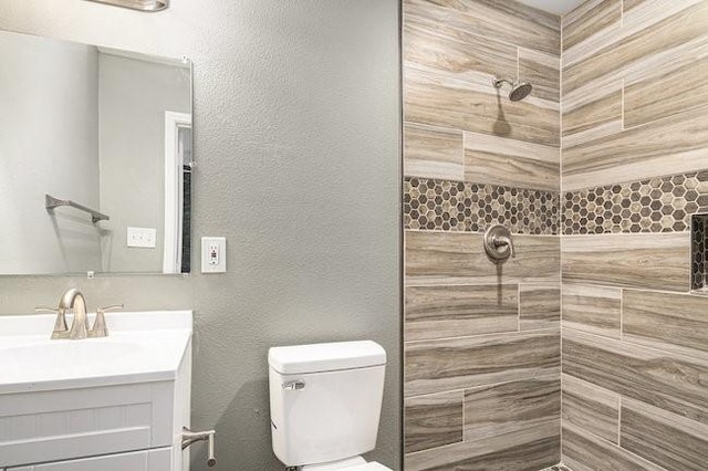 bathroom featuring vanity, toilet, a textured wall, and a tile shower