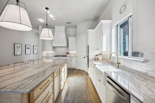 kitchen featuring light wood-style flooring, a sink, custom range hood, appliances with stainless steel finishes, and tasteful backsplash