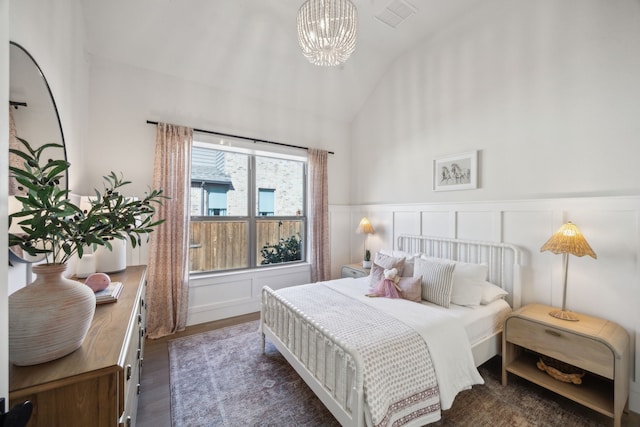 bedroom featuring wood finished floors, a wainscoted wall, visible vents, vaulted ceiling, and a decorative wall