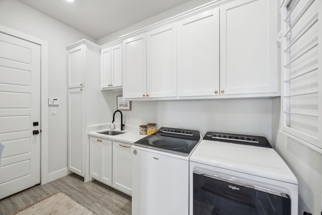 clothes washing area with cabinet space, washing machine and dryer, light wood-style floors, and a sink