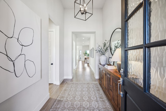 foyer with wood finished floors, baseboards, a towering ceiling, and a chandelier