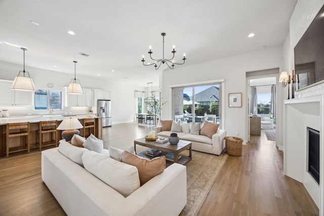 living area with visible vents, light wood-style flooring, recessed lighting, an inviting chandelier, and a fireplace