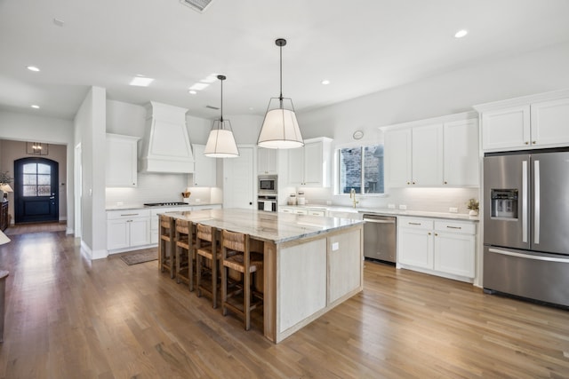 kitchen featuring light wood-style floors, custom exhaust hood, appliances with stainless steel finishes, and white cabinetry