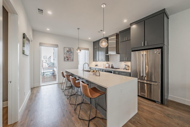 kitchen featuring visible vents, wall chimney range hood, light countertops, decorative backsplash, and appliances with stainless steel finishes