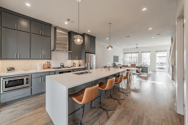 kitchen with a center island with sink, a breakfast bar, a sink, appliances with stainless steel finishes, and wall chimney exhaust hood